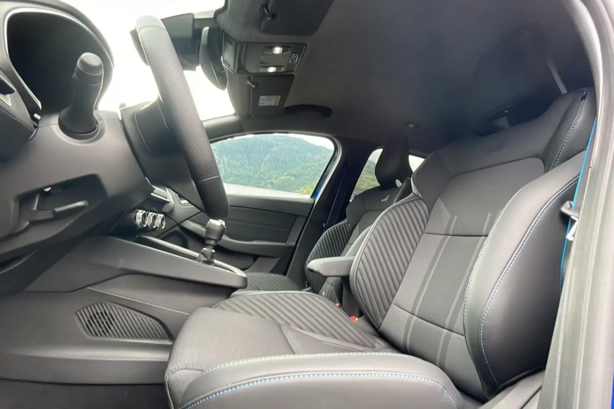 Vue intérieure côté conducteur de la Renault Clio V TCE 90 Esprit Alpine 2025 avec sièges sport noirs et surpiqûres bleues.