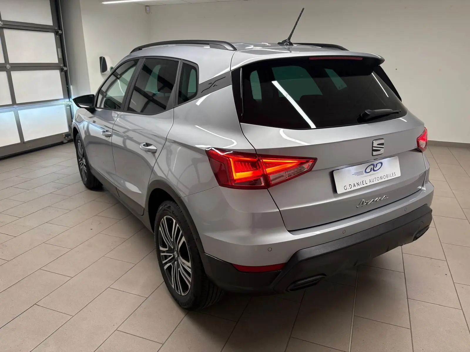 SEAT Arona gris urbain en 3/4 arrière droit, vitres arrière surteintées et feux arrière allumés en intérieur showroom.
