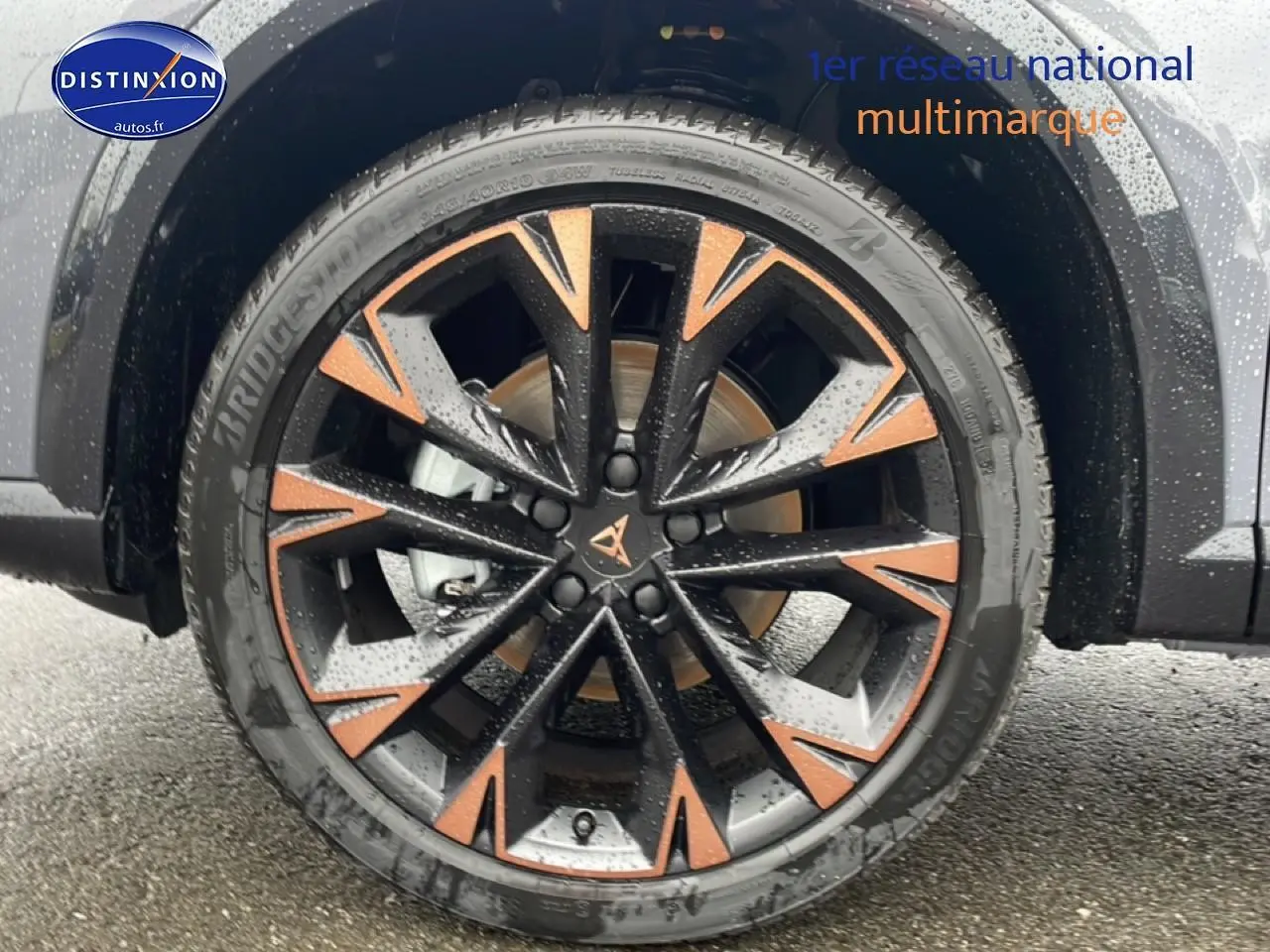 Gros plan sur la jante noire et cuivre du CUPRA Formentor gris graphene, avec pneu Bridgestone humide.