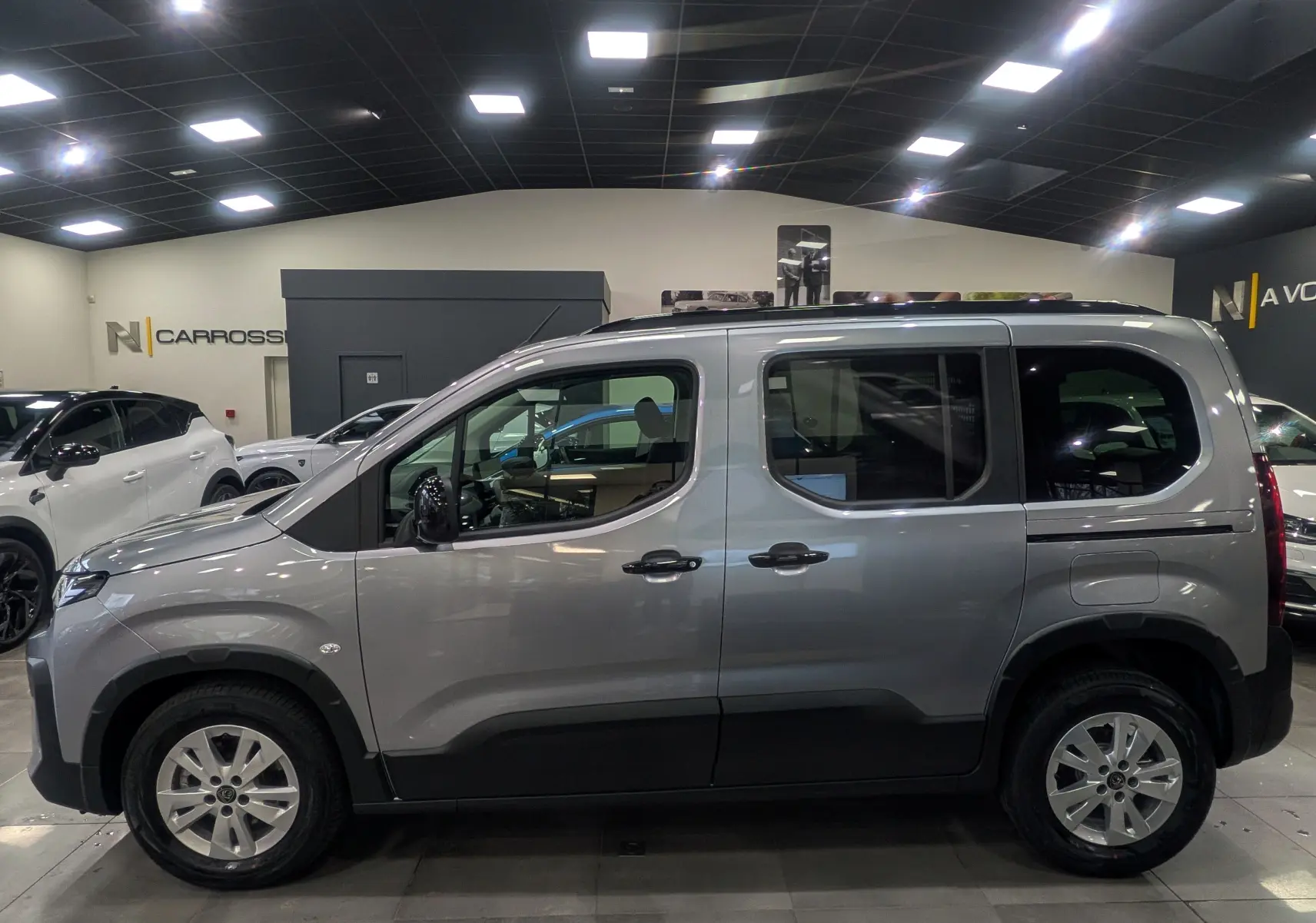 Vue de profil côté gauche d’un Peugeot Rifter gris acier 2025 en intérieur, avec jantes alliage et vitres teintées.