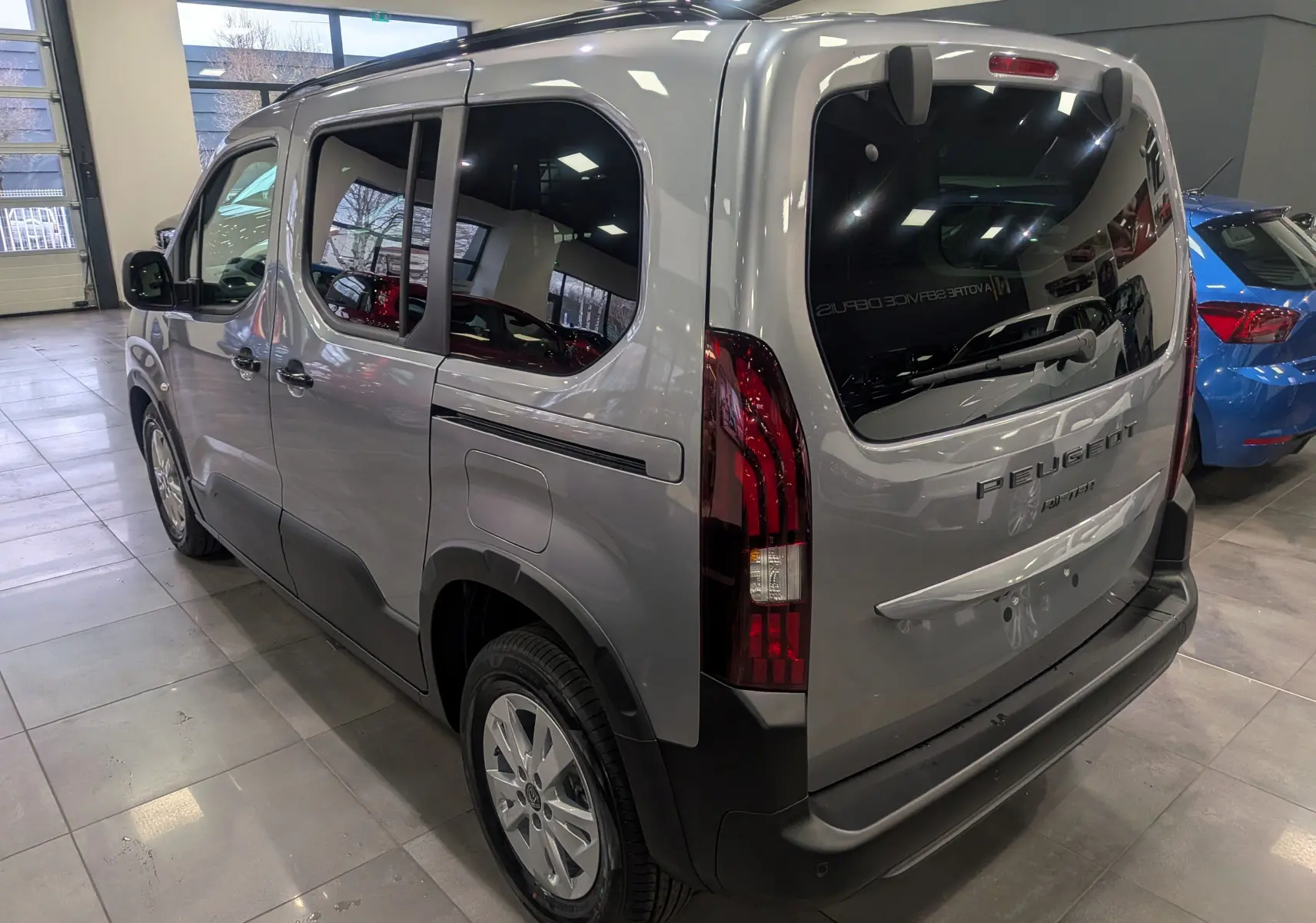 Vue 3/4 arrière droite du Peugeot Rifter 2025 gris acier avec vitres teintées et feux arrière verticaux distinctifs.