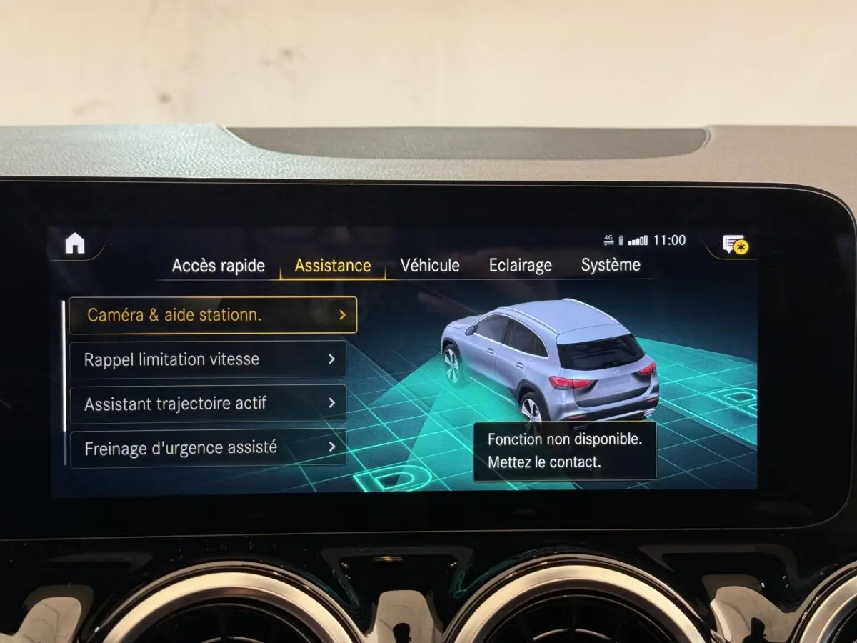 Écran tactile intérieur affichant l'assistance au stationnement avec vue 3D d'un Mercedes GLA gris clair en 3/4 arrière.