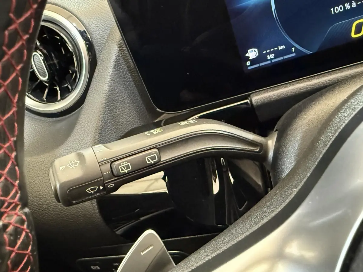 Gros plan sur la manette d'essuie-glace à gauche du volant avec volant cuir noir sur fond de tableau de bord numérique.