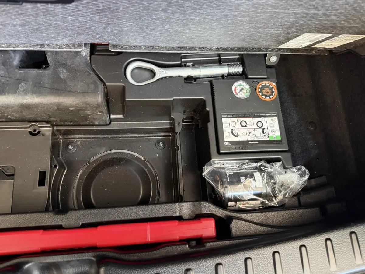 Vue rapprochée du compartiment de rangement sous le coffre du Mercedes GLA 250 e AMG Line gris clair, montrant outils et compresseur.
