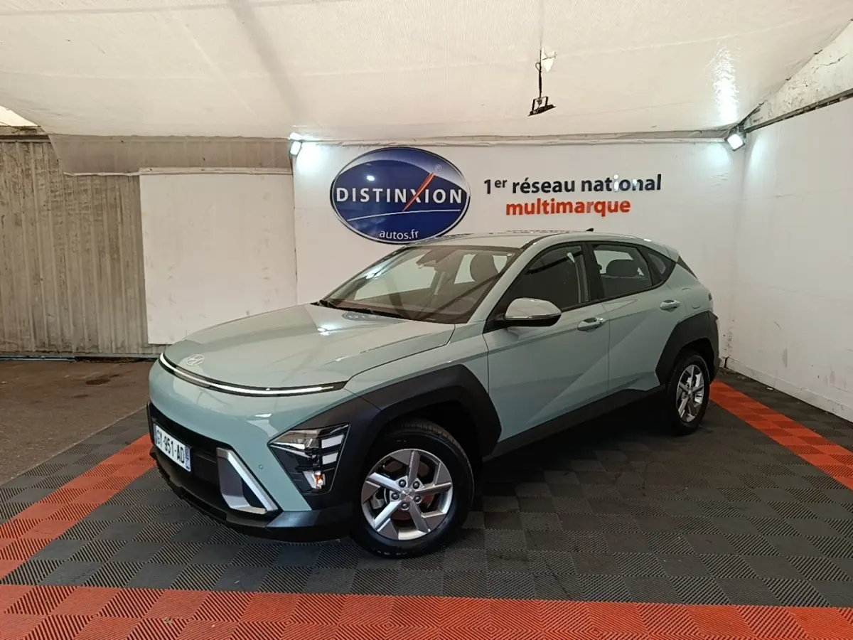 Vue 3/4 avant droite d’un Hyundai Kona 2024 vert clair avec protections noires et jantes alliage en intérieur showroom.
