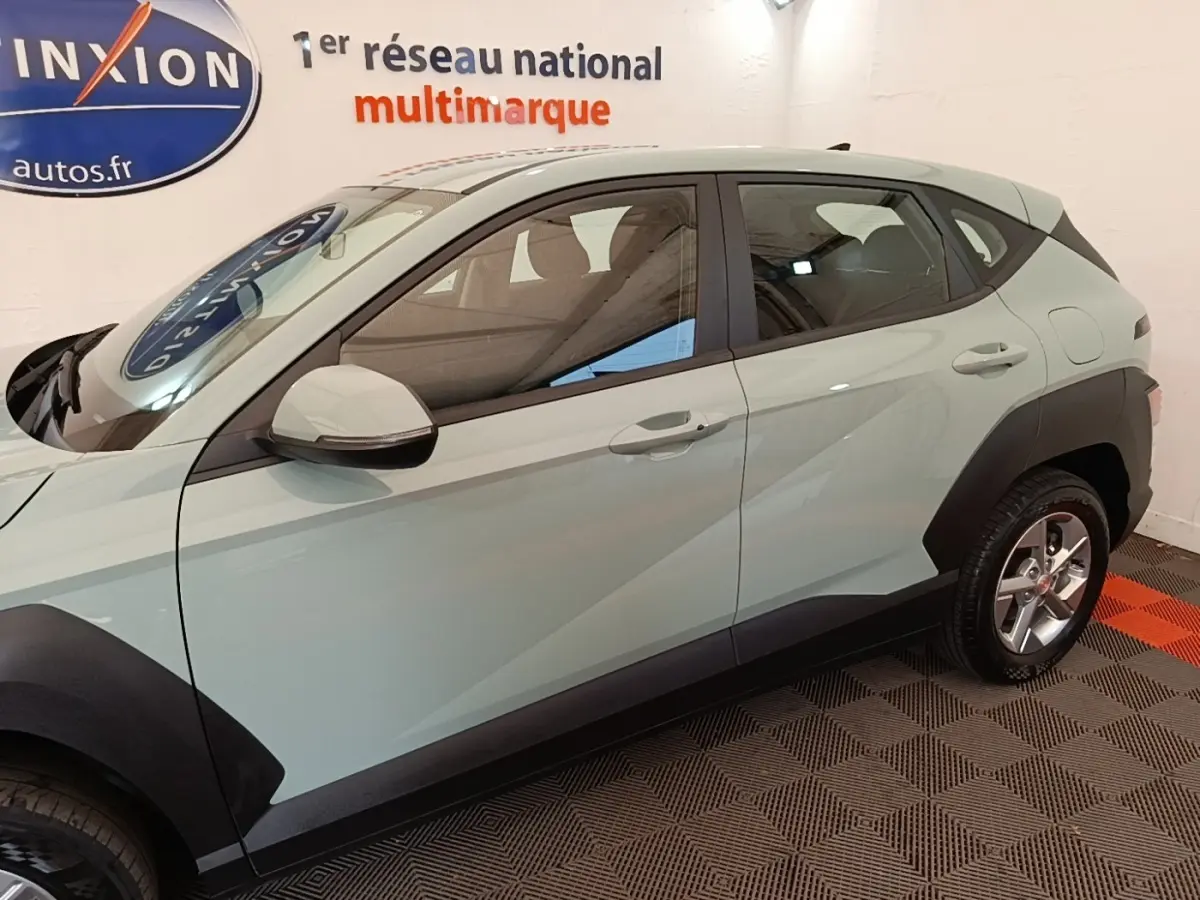Vue de profil côté gauche d’un Hyundai Kona vert 2024 avec protections noires sur les passages de roues.