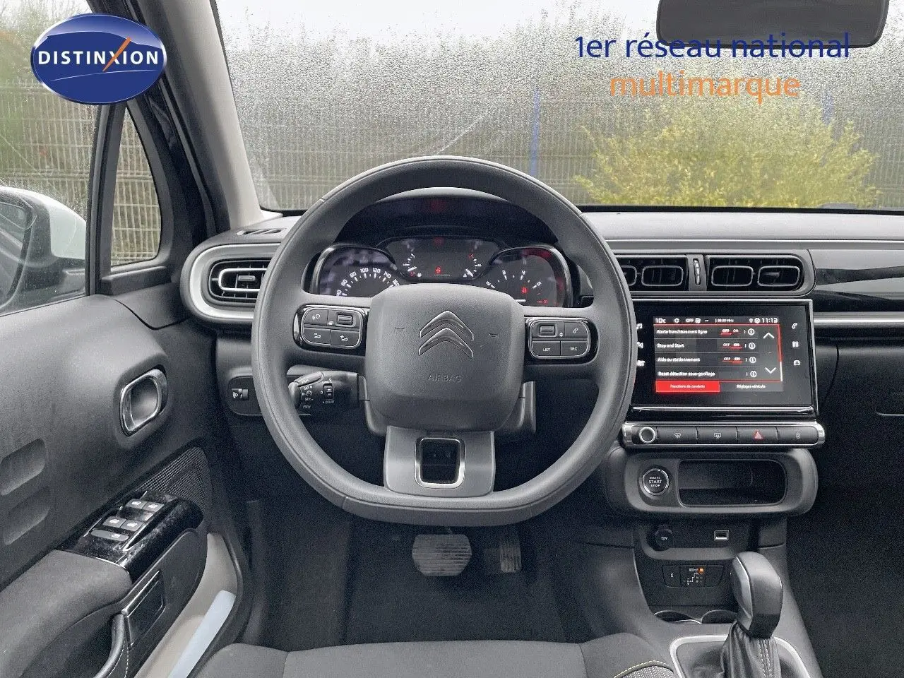 Vue intérieure centrée sur le volant et le tableau de bord d'une Citroën C3 noire métal 2023 avec écran tactile allumé.