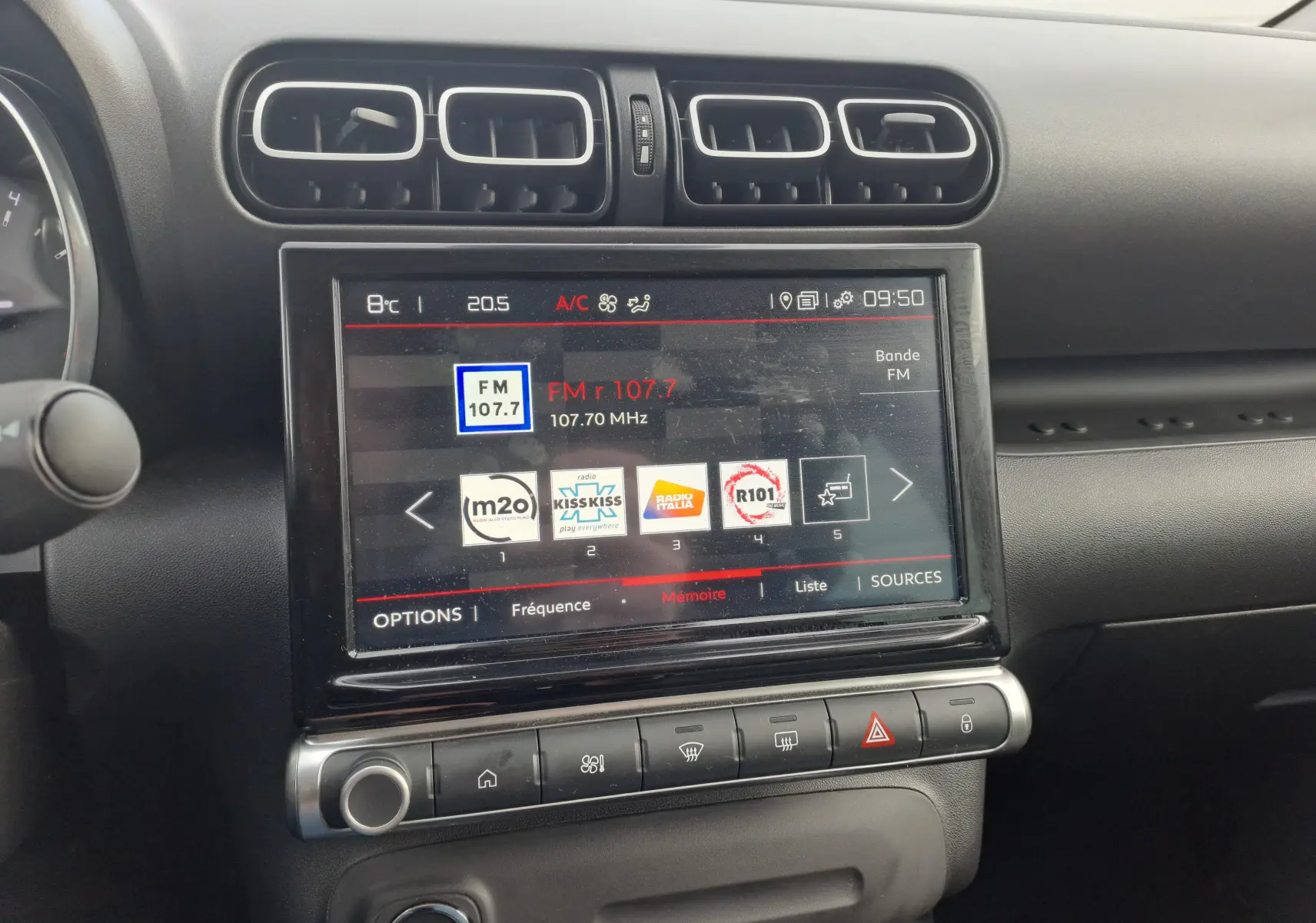 Vue rapprochée de l’écran tactile central noir du Citroën C3 Aircross blanc banquise 2024 affichant la radio FM et les commandes climatiques.