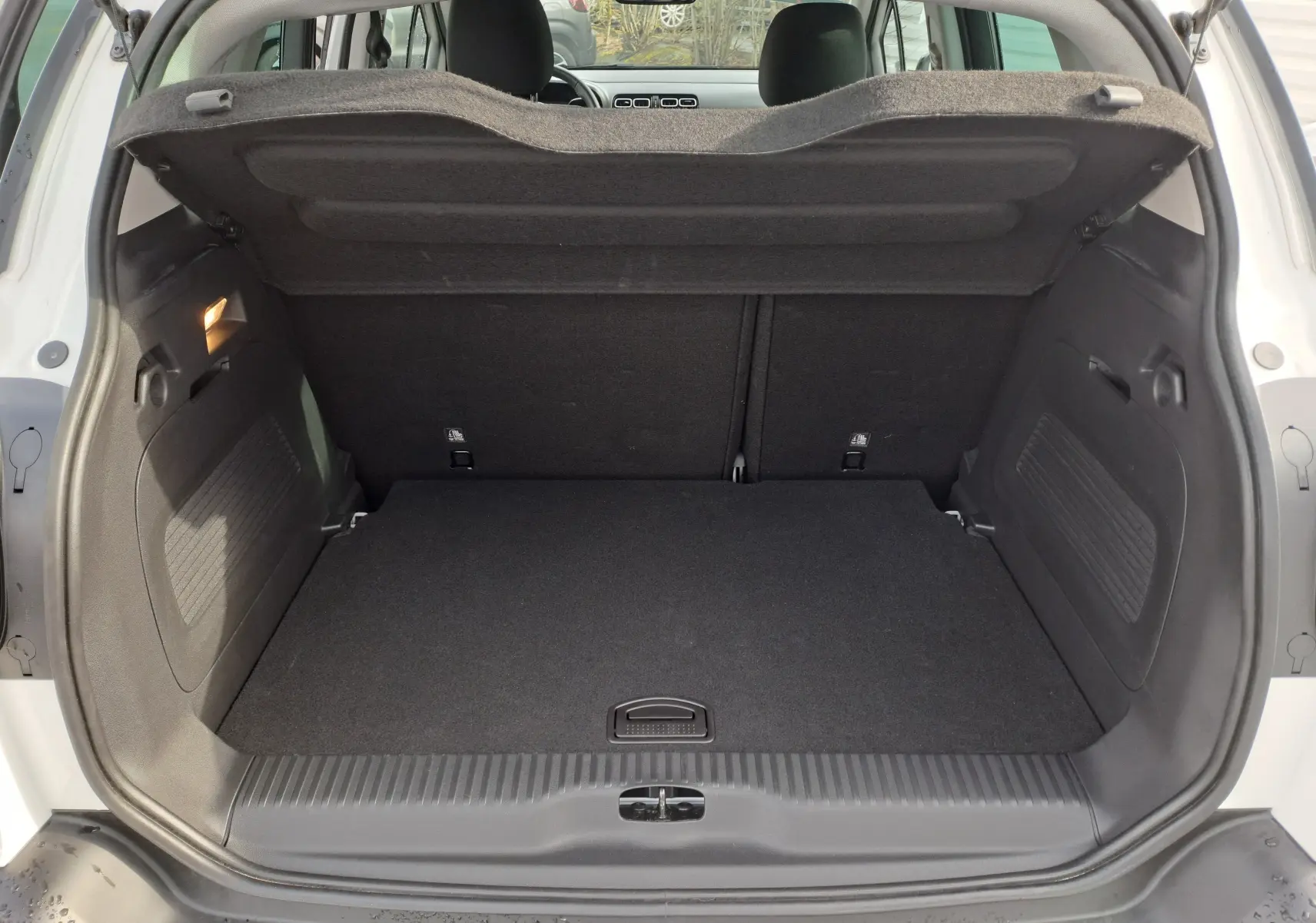 Coffre ouvert vu de l'arrière d'une Citroën C3 Aircross blanc banquise, intérieur noir et tablette de coffre relevée.