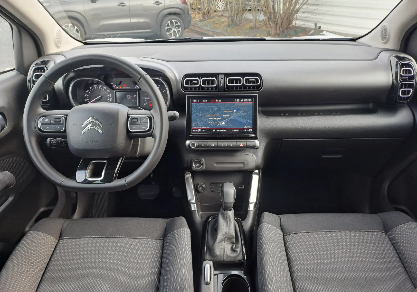 Vue intérieure frontale du tableau de bord et volant noir du Citroën C3 Aircross blanc banquise 2024 avec écran tactile central et boîte auto.