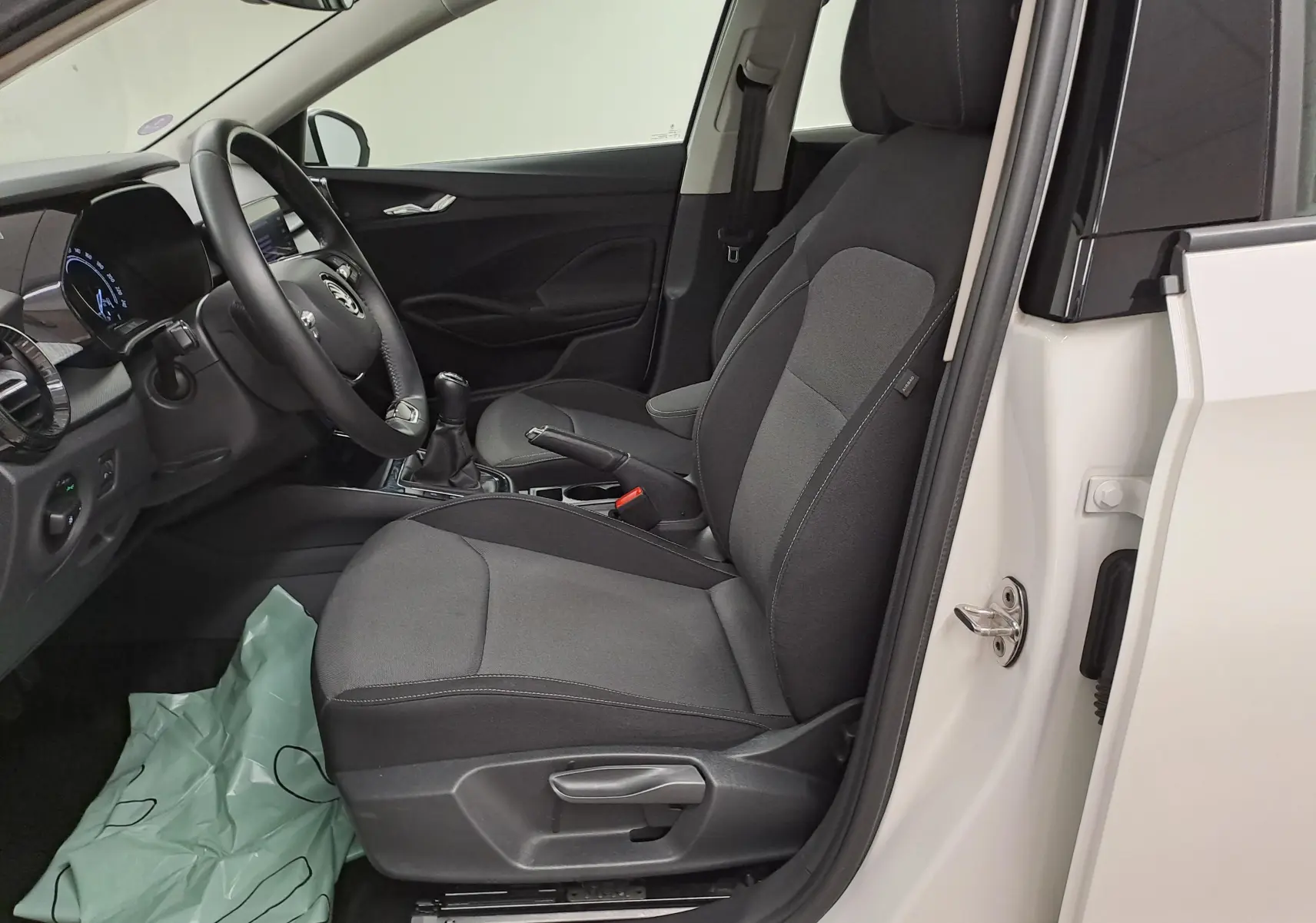 Intérieur côté conducteur d'une Skoda Fabia 2023 blanc candy, montrant siège tissu gris et tableau de bord moderne.