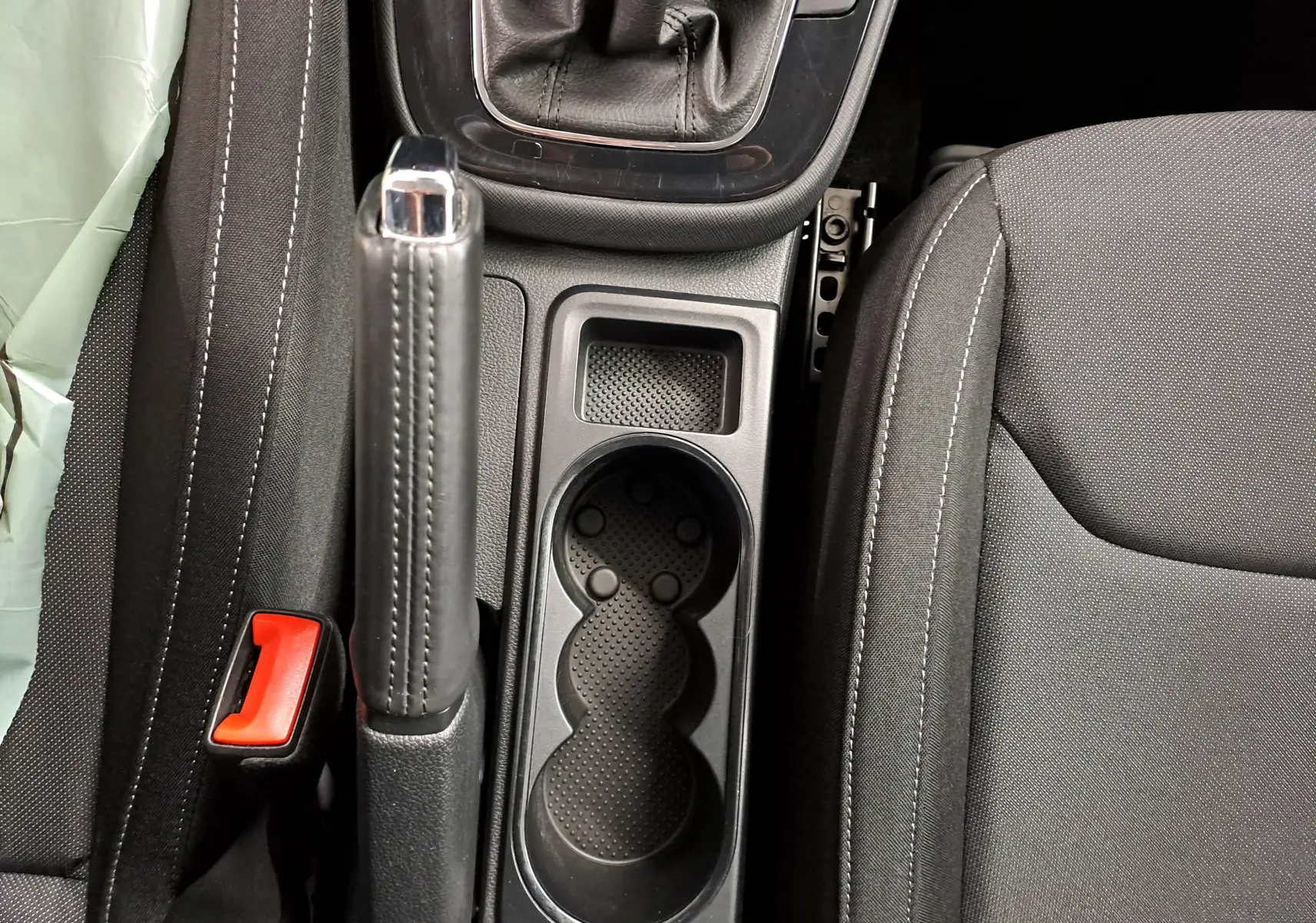 Gros plan sur la console centrale noire de la Skoda Fabia 2023, avec frein à main, porte-gobelets et siège tissu gris.