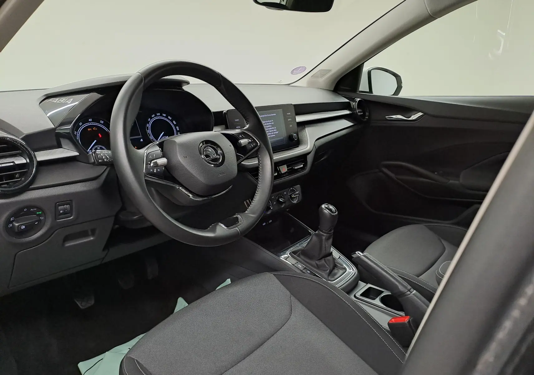 Intérieur noir de la Skoda Fabia 2023, vue côté conducteur montrant le volant, tableau de bord et levier de vitesses manuel.