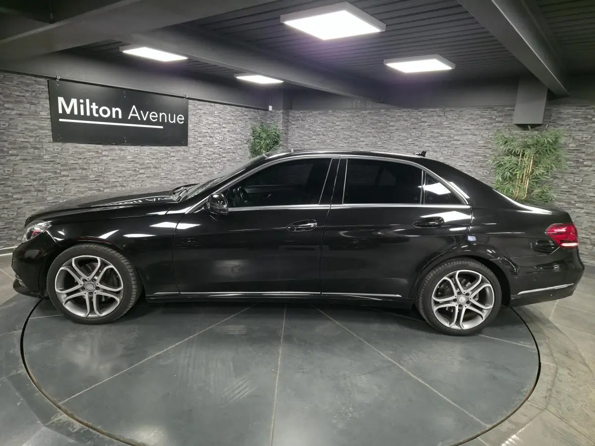 Profil côté gauche d'une Mercedes Classe E 300 BlueTEC Hybrid noire avec jantes alliage 18 pouces en intérieur showroom.
