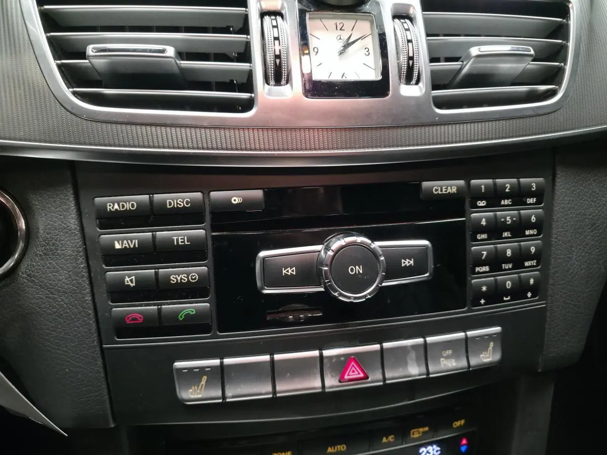 Tableau de bord Mercedes Classe E 2015 noir, vue centrée sur console centrale avec horloge analogique et commandes multimédia.