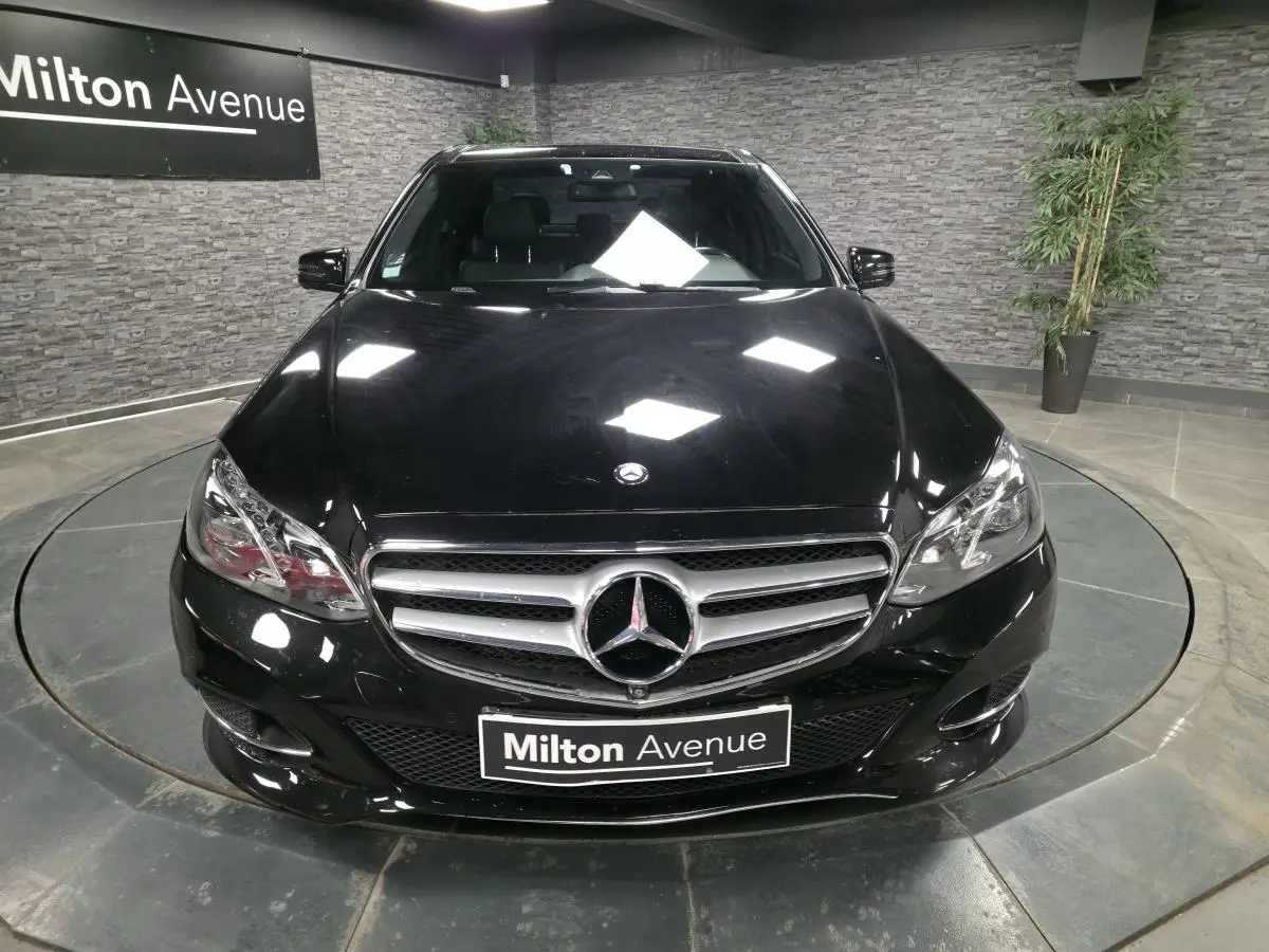 Vue avant d'une Mercedes Classe E noire avec calandre chromée et logo étoile centrale, en showroom intérieur.