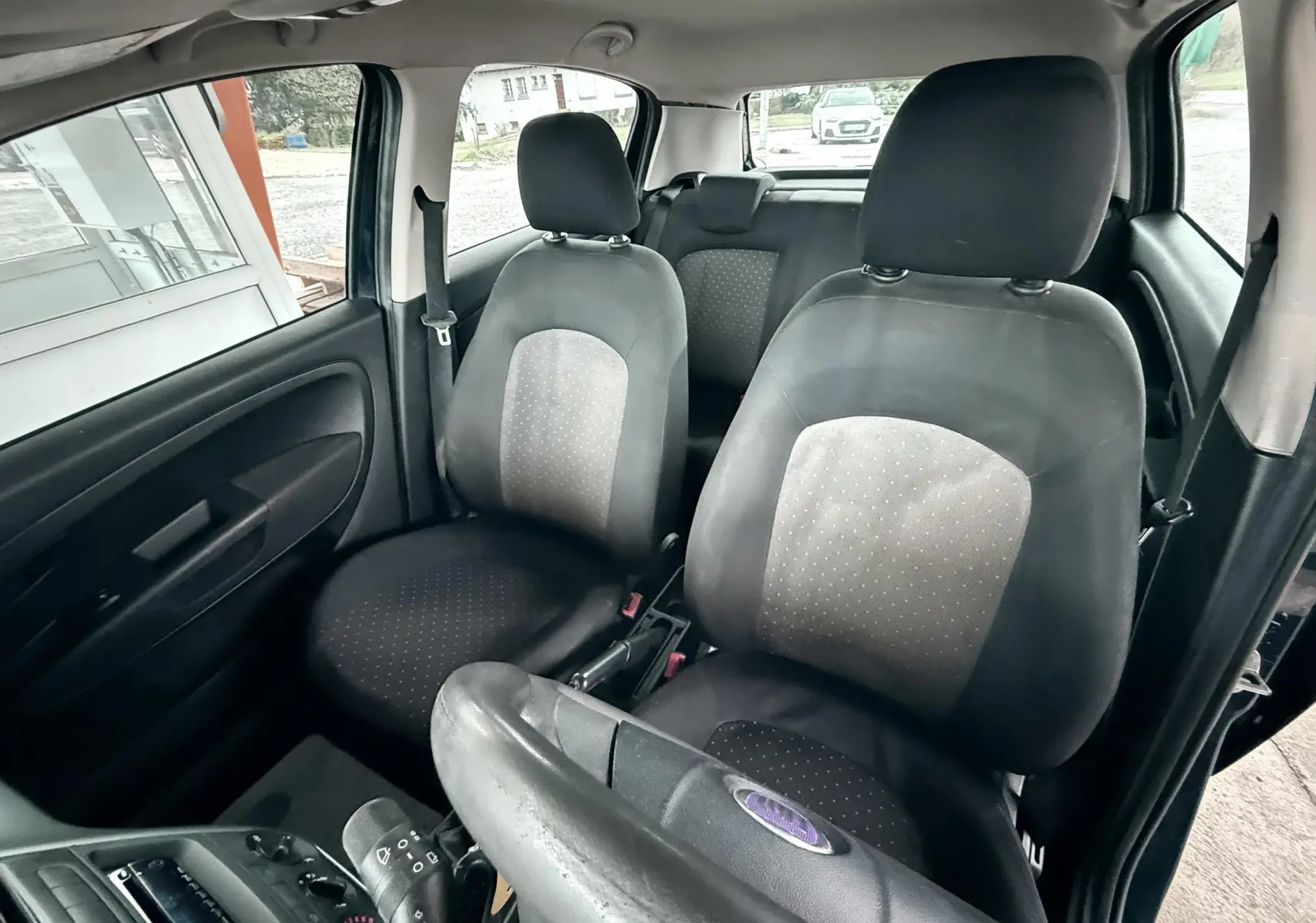 Vue intérieure côté avant gauche de la Fiat Punto noire 2009, montrant les sièges avant en tissu bicolore.