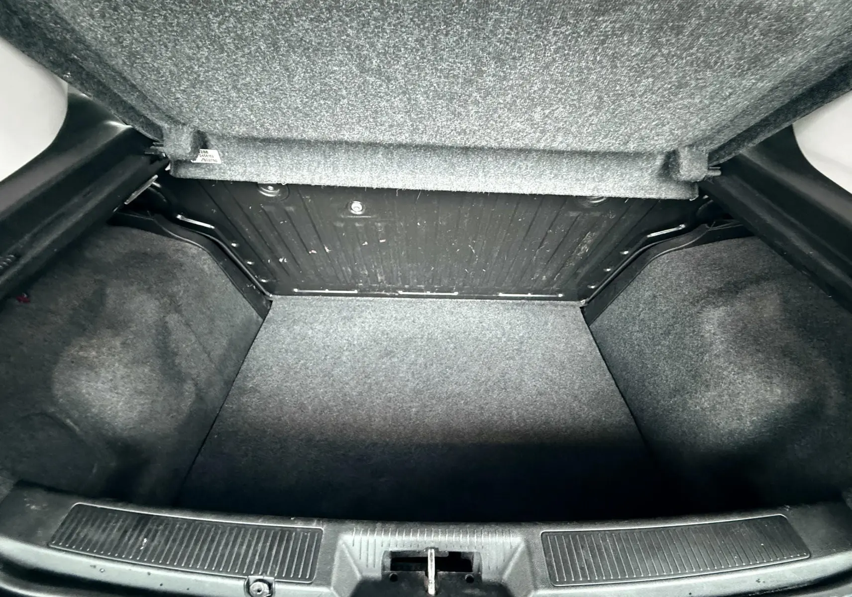 Coffre ouvert de la Fiat Punto 1.2 i 65 noire de 2009, montrant l’espace de rangement vide et la moquette grise.