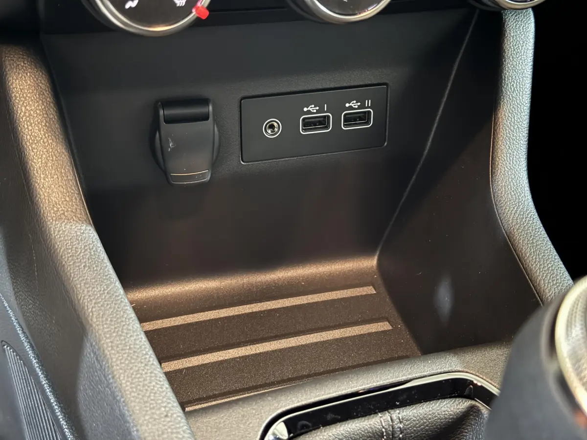 Gros plan sur la console centrale noire de la Renault Clio gris clair, montrant deux ports USB et une prise 12V.