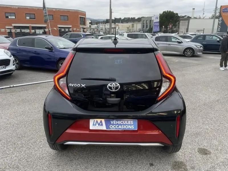 Vue arrière d'une Toyota Aygo X 2023 rouge piment avec toit noir, feux arrière en forme de C lumineux.