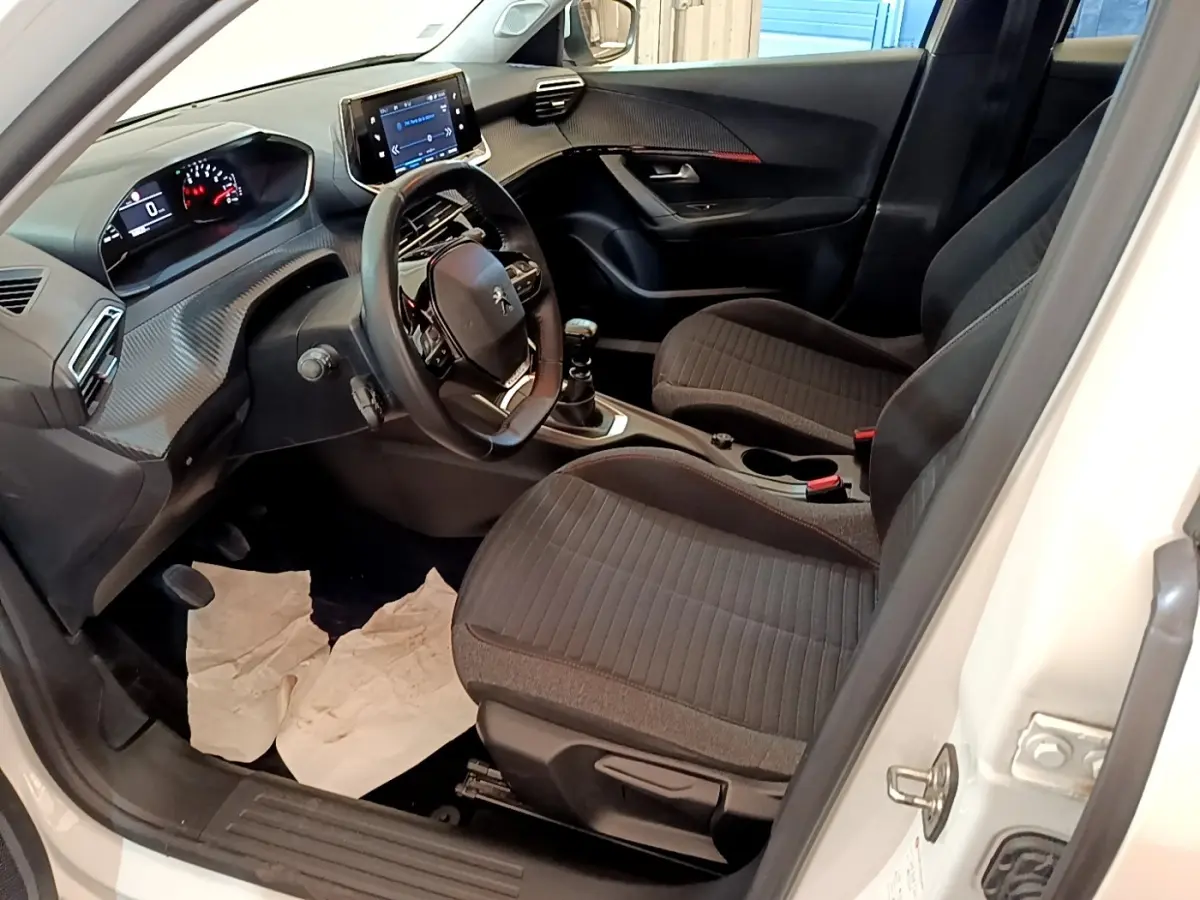 Vue intérieure côté conducteur du Peugeot 2008 blanc, montrant le volant cuir, tableau de bord et écran tactile central.