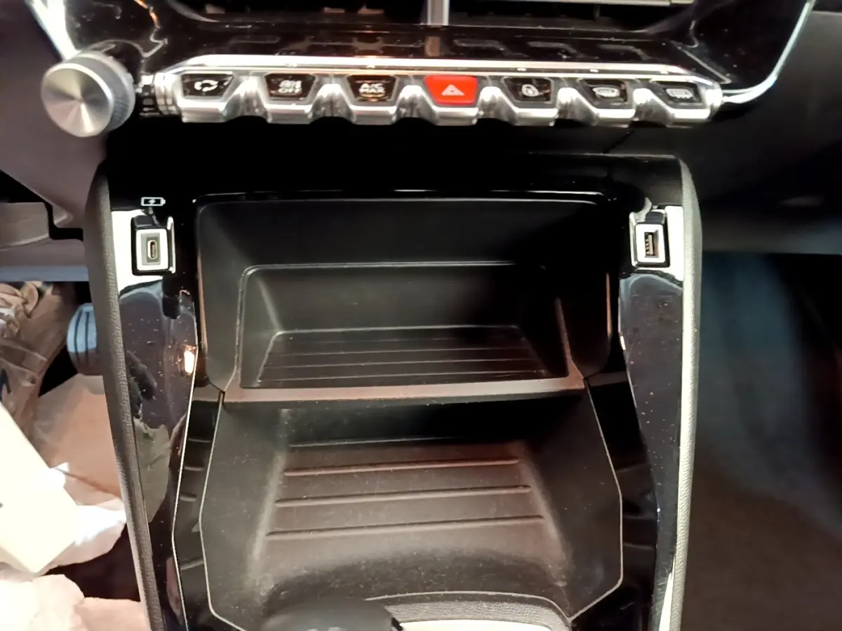 Gros plan sur la console centrale noire de la Peugeot 2008 blanche, avec boutons de commande et ports USB visibles.