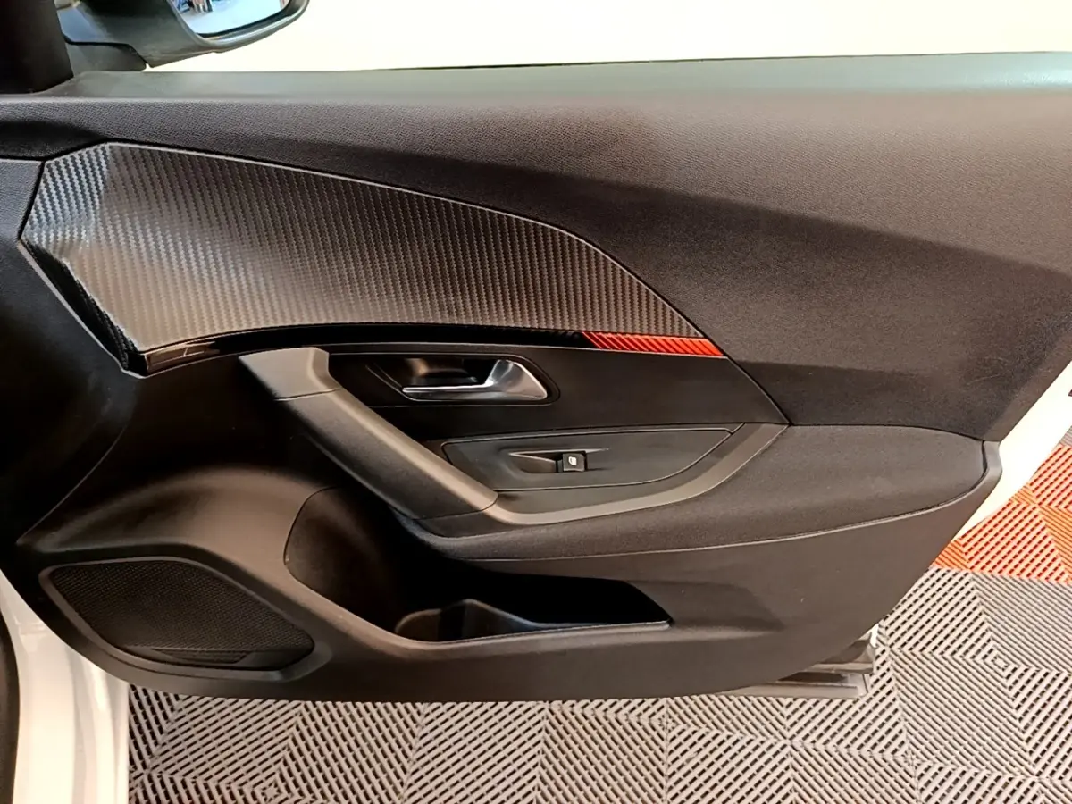 Vue intérieure côté gauche de la porte d’une Peugeot 2008 blanche avec insert décor carbone et bouton de lève-vitre.