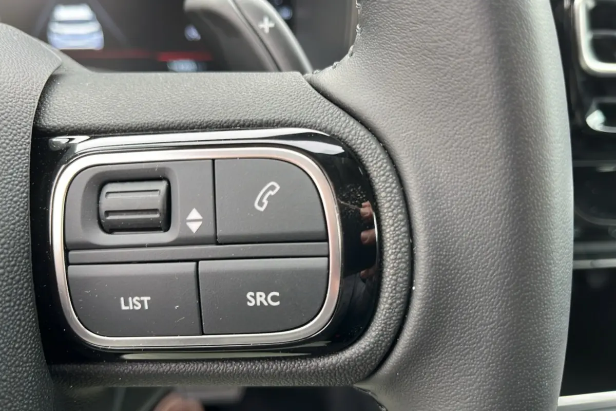 Gros plan sur les commandes multifonctions gauche du volant cuir noir du Citroën C5 Aircross Hybrid 2025.