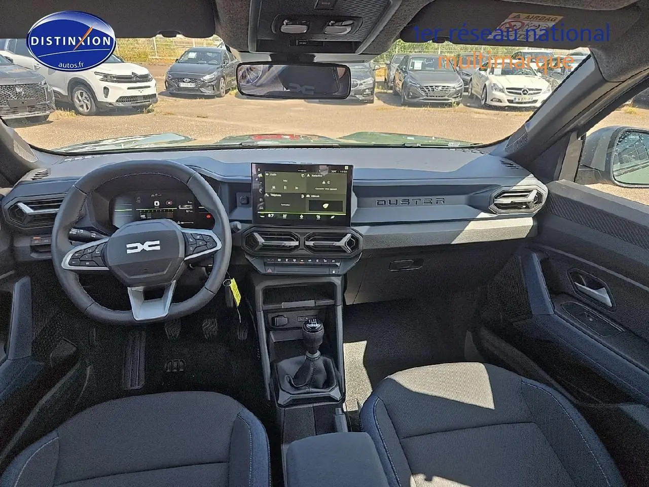 Vue intérieure avant du Dacia Duster 2025, tableau de bord gris avec écran tactile et volant multifonction noir.