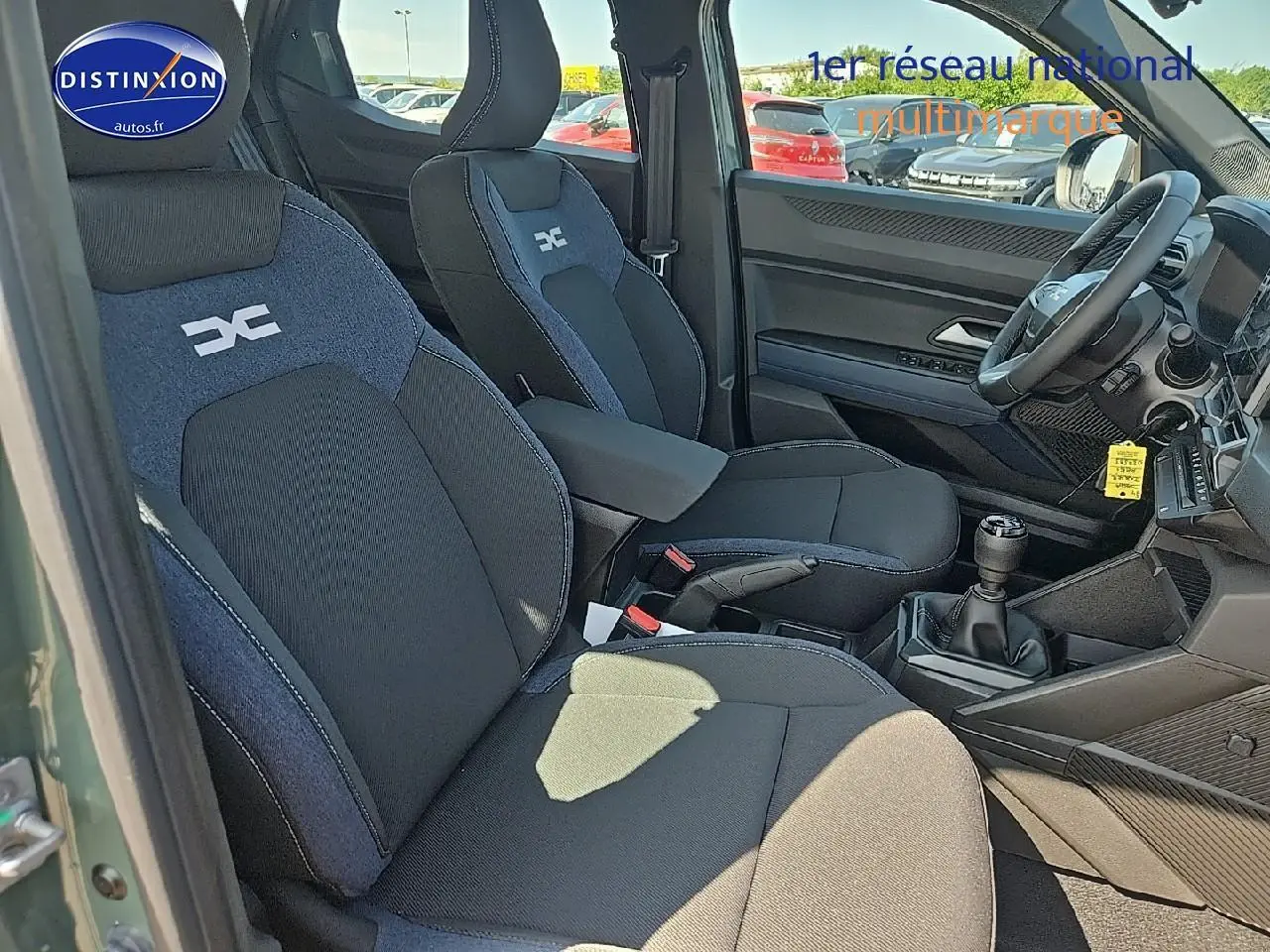 Vue intérieure côté conducteur du Dacia Duster 2025 vert kaki, sièges tissu noir et bleu avec logo distinctif, volant multifonction.