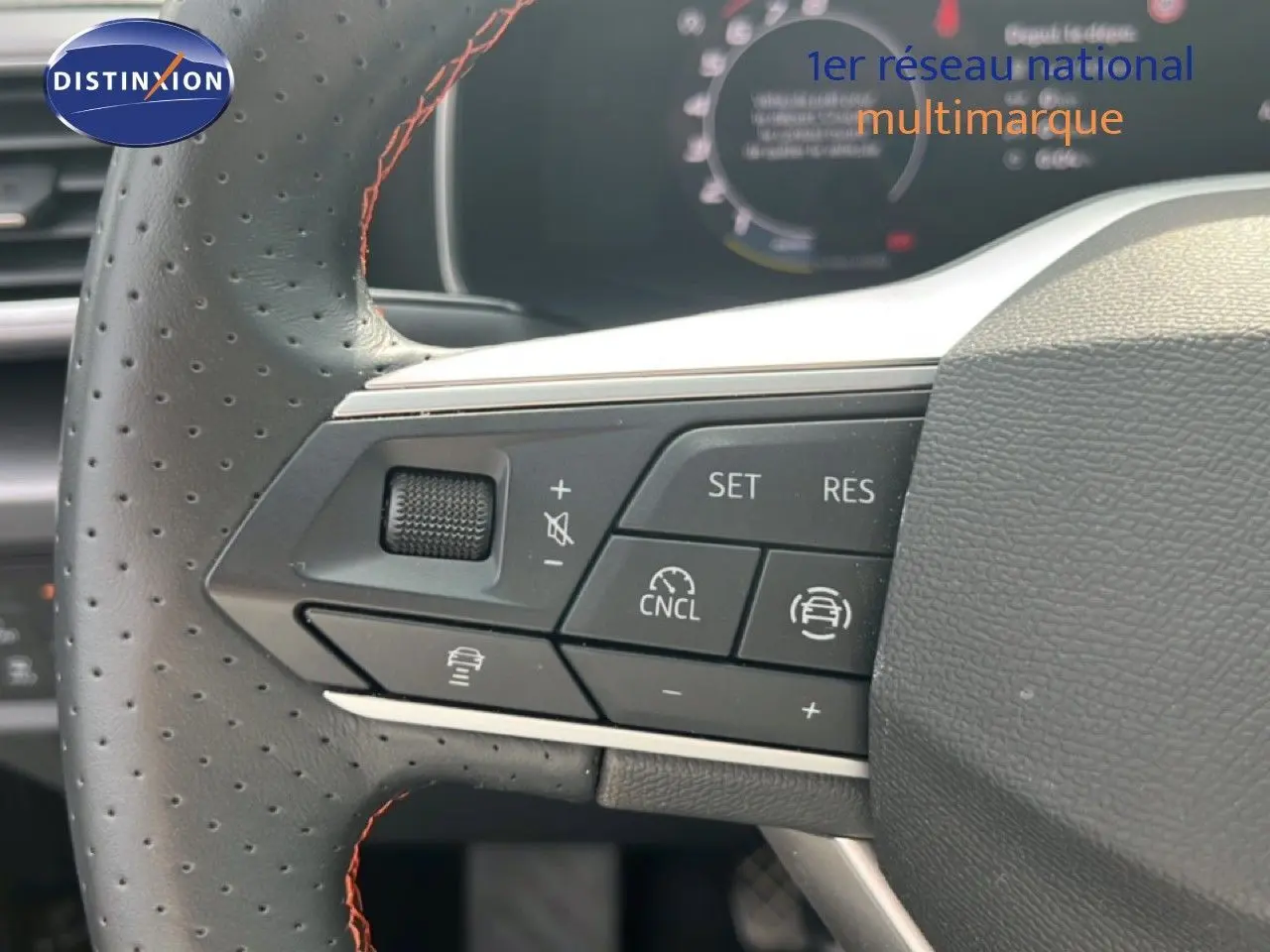 Gros plan sur le volant perforé avec surpiqûres rouges du SEAT LEON ST gris magnétique, boutons de commande visibles.