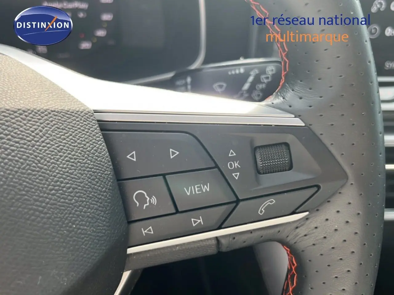 Gros plan sur les commandes du volant perforé avec surpiqûres rouges d'une SEAT LEON ST gris magnétique 2025.