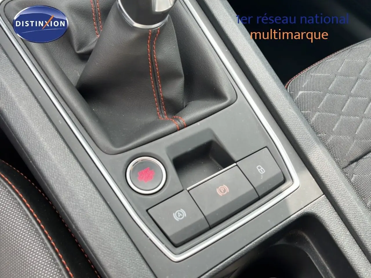 Gros plan sur la console centrale de la SEAT LEON ST 2025, avec levier de vitesse manuel et surpiqûres rouges.