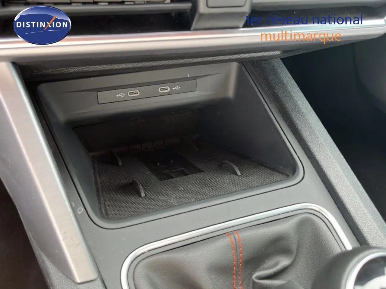 Gros plan sur la console centrale de la SEAT LEON ST 2025, montrant le rangement avec ports USB et soufflet de levier de vitesse noir.