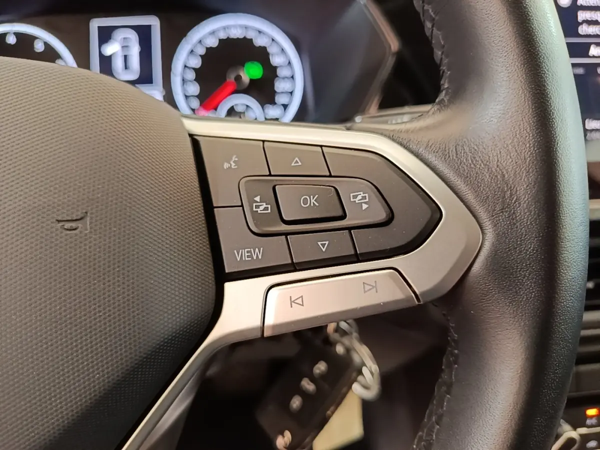 Gros plan sur le volant cuir noir du Volkswagen T-Cross 2022, avec commandes multifonctions et tableau de bord partiellement visible.