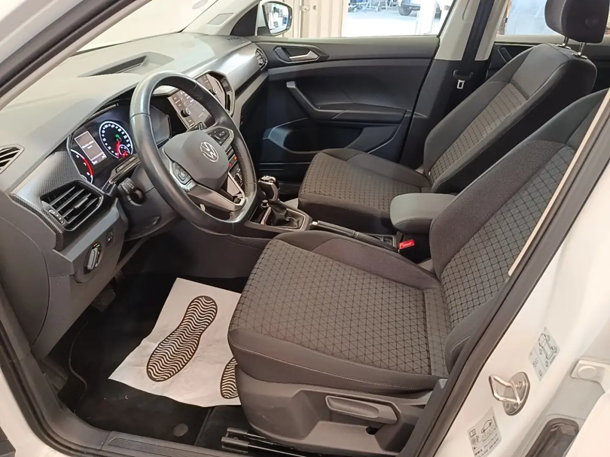 Vue intérieure côté conducteur du Volkswagen T-Cross blanc, montrant sièges tissu gris et tableau de bord moderne.