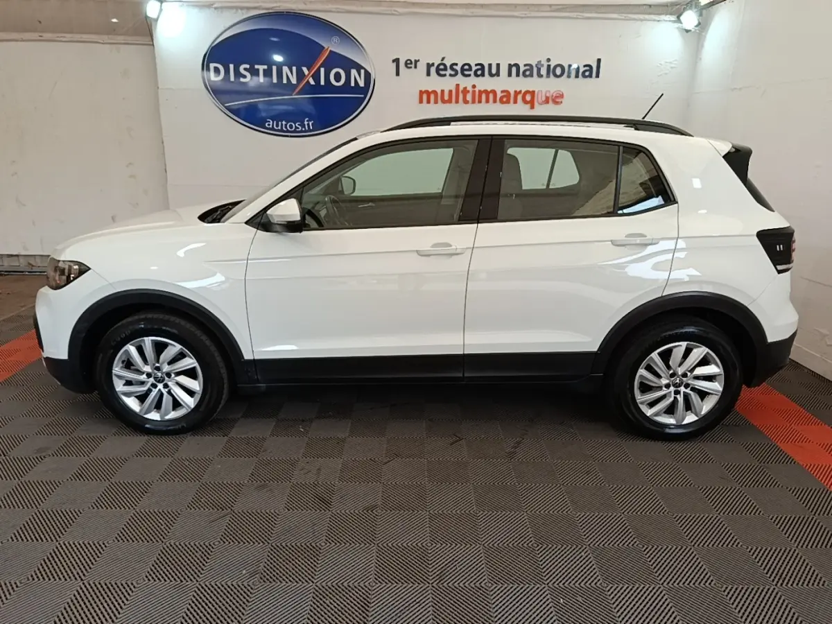 Profil droit d'un Volkswagen T-Cross blanc 2022 avec jantes alliage et barres de toit noires en intérieur showroom.