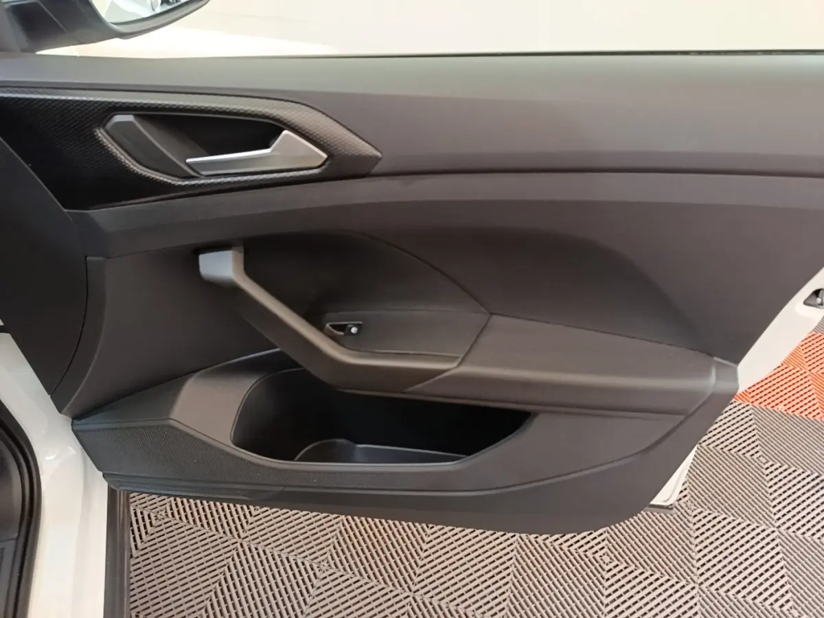 Vue intérieure côté gauche de la porte avant d’un Volkswagen T-Cross blanc avec poignée argentée et rangement intégré.