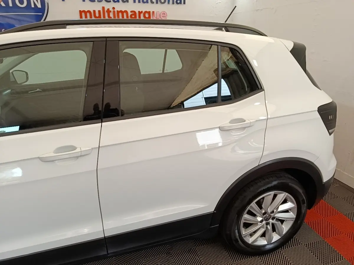 Vue latérale droite d'un Volkswagen T-Cross blanc, mettant en valeur la roue arrière et les vitres teintées.
