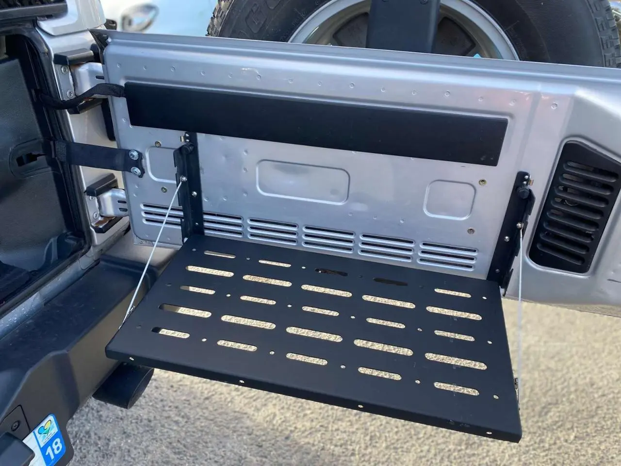 Vue rapprochée de la porte arrière ouverte gris clair du Jeep Wrangler 2012 avec tablette rabattable noire intégrée.