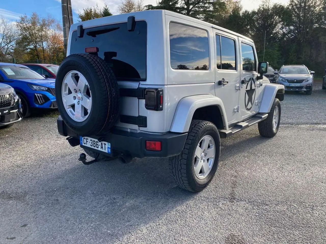 Jeep Wrangler 2.8 CRD 200 Unlimited gris clair vue 3/4 arrière droit avec roue de secours et étoile noire sur porte.