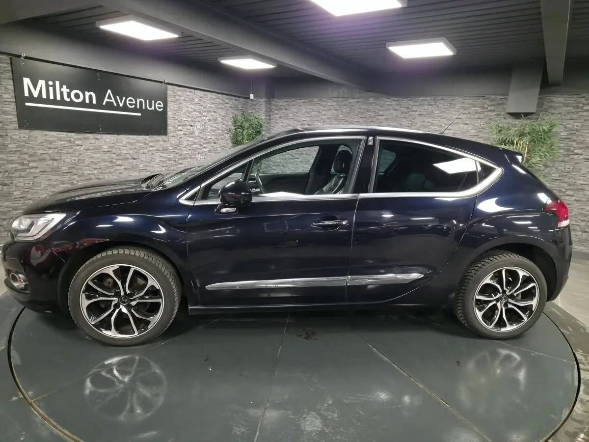 Profil côté gauche d'une DS4 violet foncé métallisé avec jantes alliage et poignées chromées en intérieur showroom.