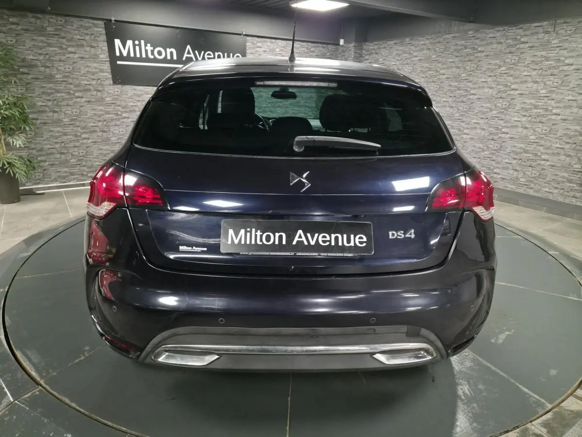 Vue arrière d'une DS4 violet foncé avec feux rouges et double sortie d'échappement chromée dans un showroom.