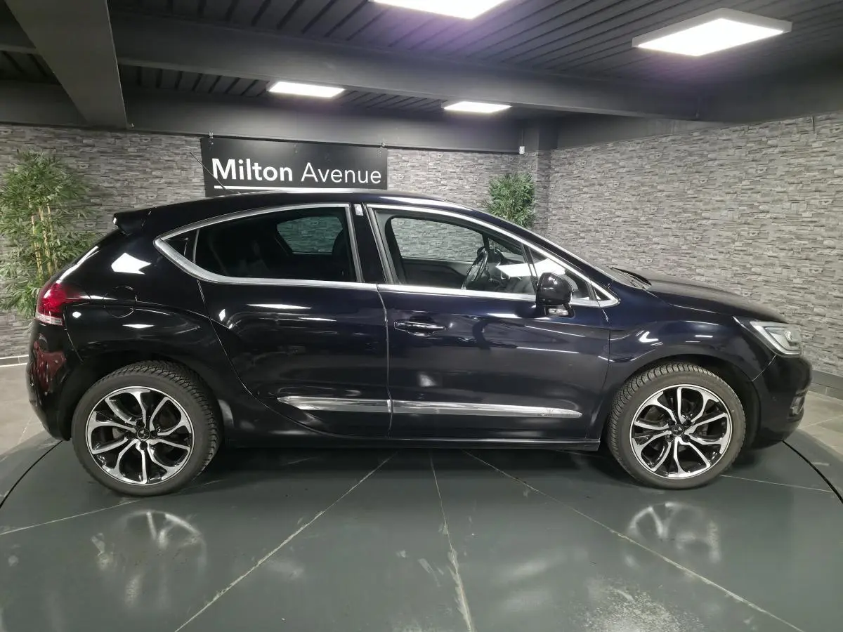 Profil droit d'une DS4 violet métallisé avec jantes alliage noires et baguettes chromées dans un showroom intérieur.