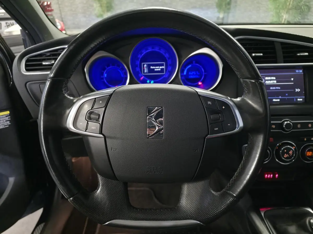 Volant cuir noir avec logo DS au centre, tableau de bord éclairé en bleu et console centrale d'une DS4 violet diesel 2016.