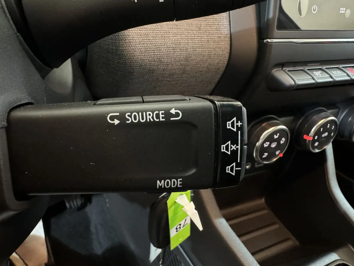 Gros plan sur la commande multimédia au volant de la Renault Clio gris clair, avec boutons source et mode visibles.