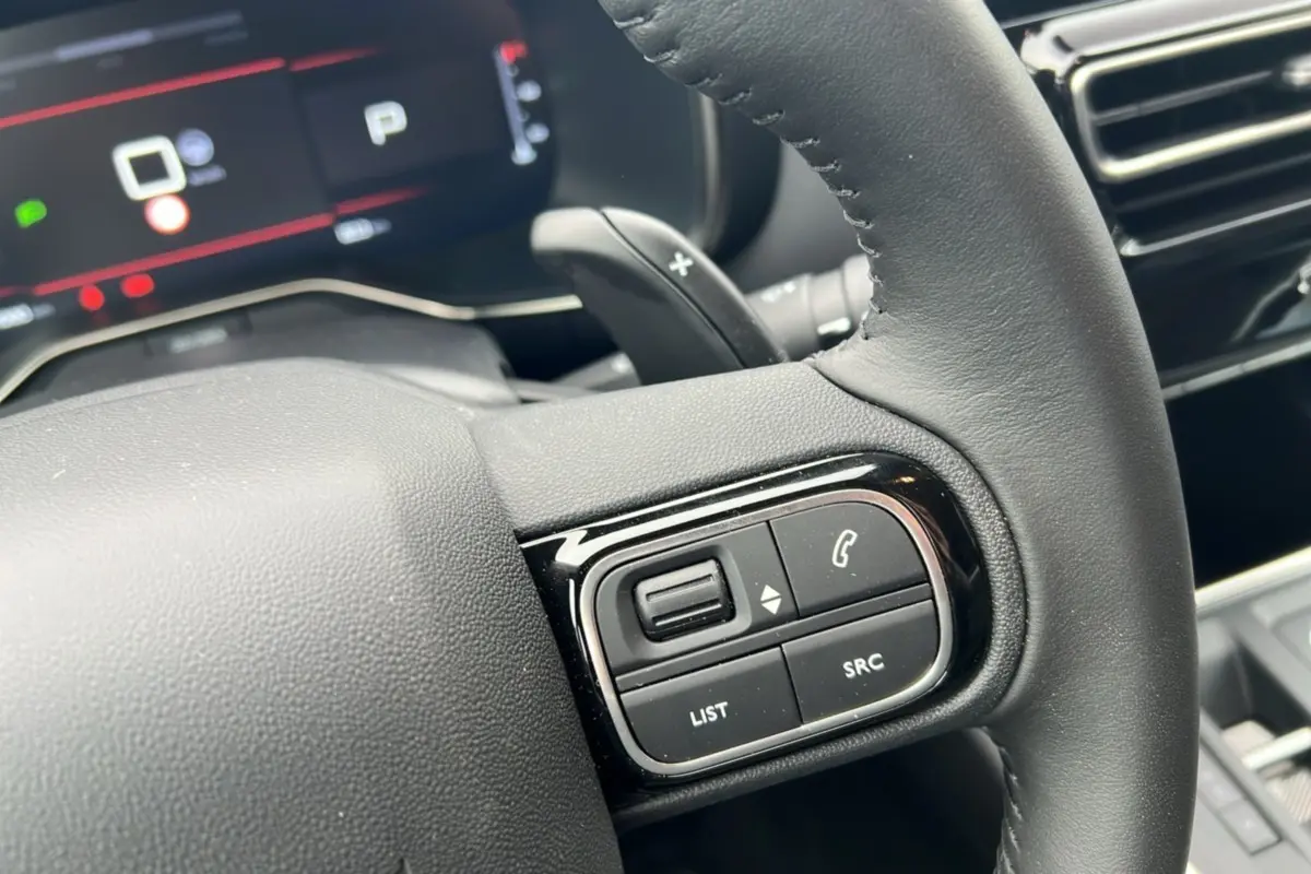 Gros plan sur le volant cuir noir du Citroën C5 Aircross Hybrid 145, avec commandes audio et palettes au volant visibles.
