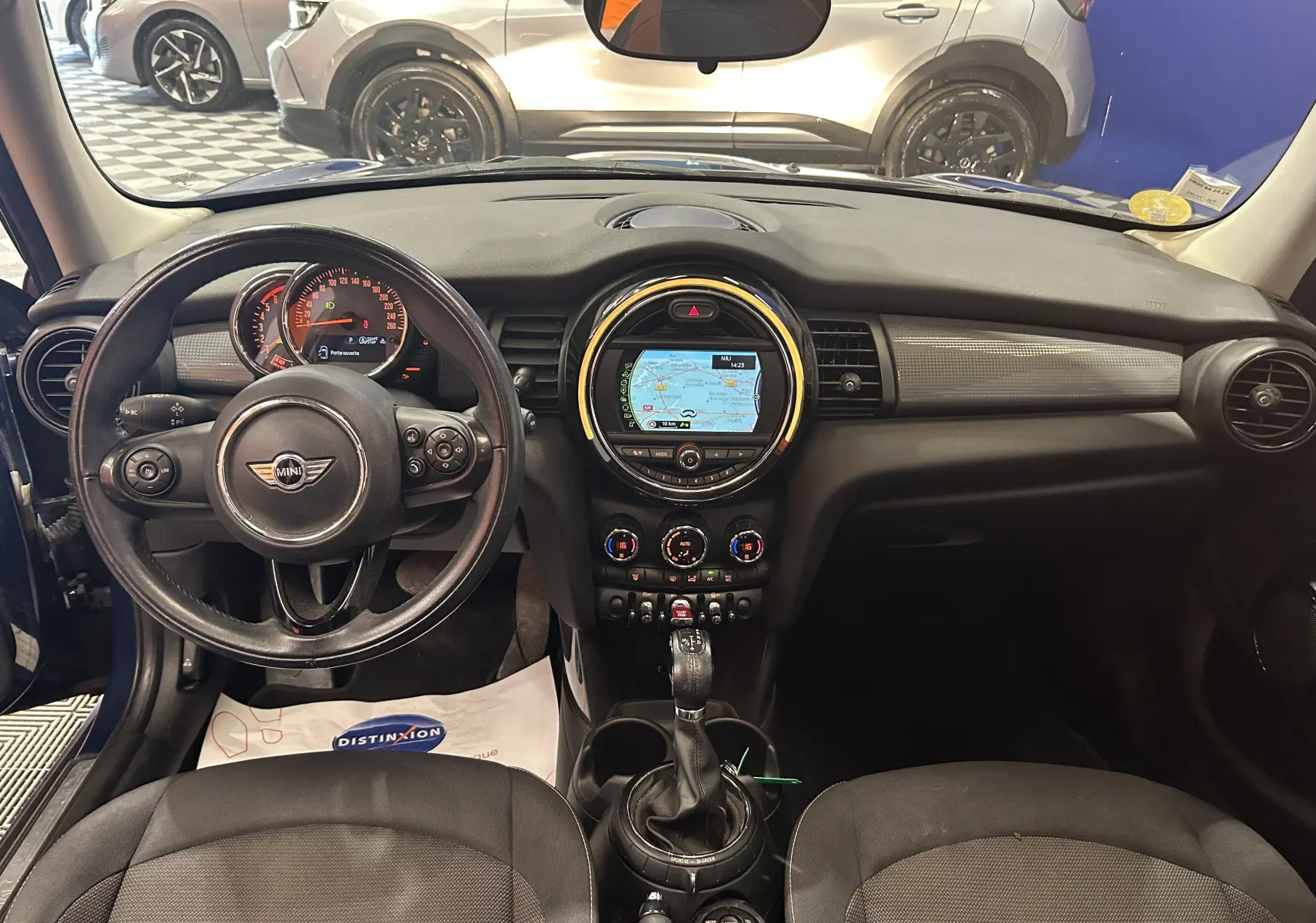 Vue intérieure du tableau de bord de la MINI 5P Cooper D bleu, avec volant cuir et écran GPS central allumé.