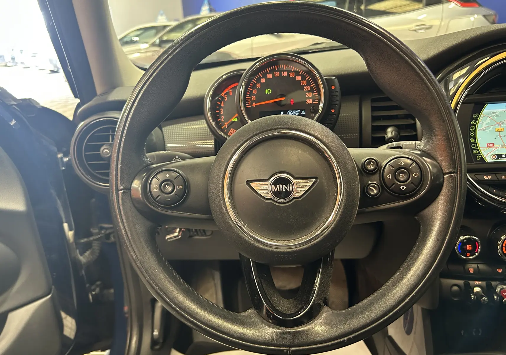 Vue centrée sur le volant en cuir noir de la MINI 5P Cooper D 2015, avec tableau de bord et écran GPS visibles.