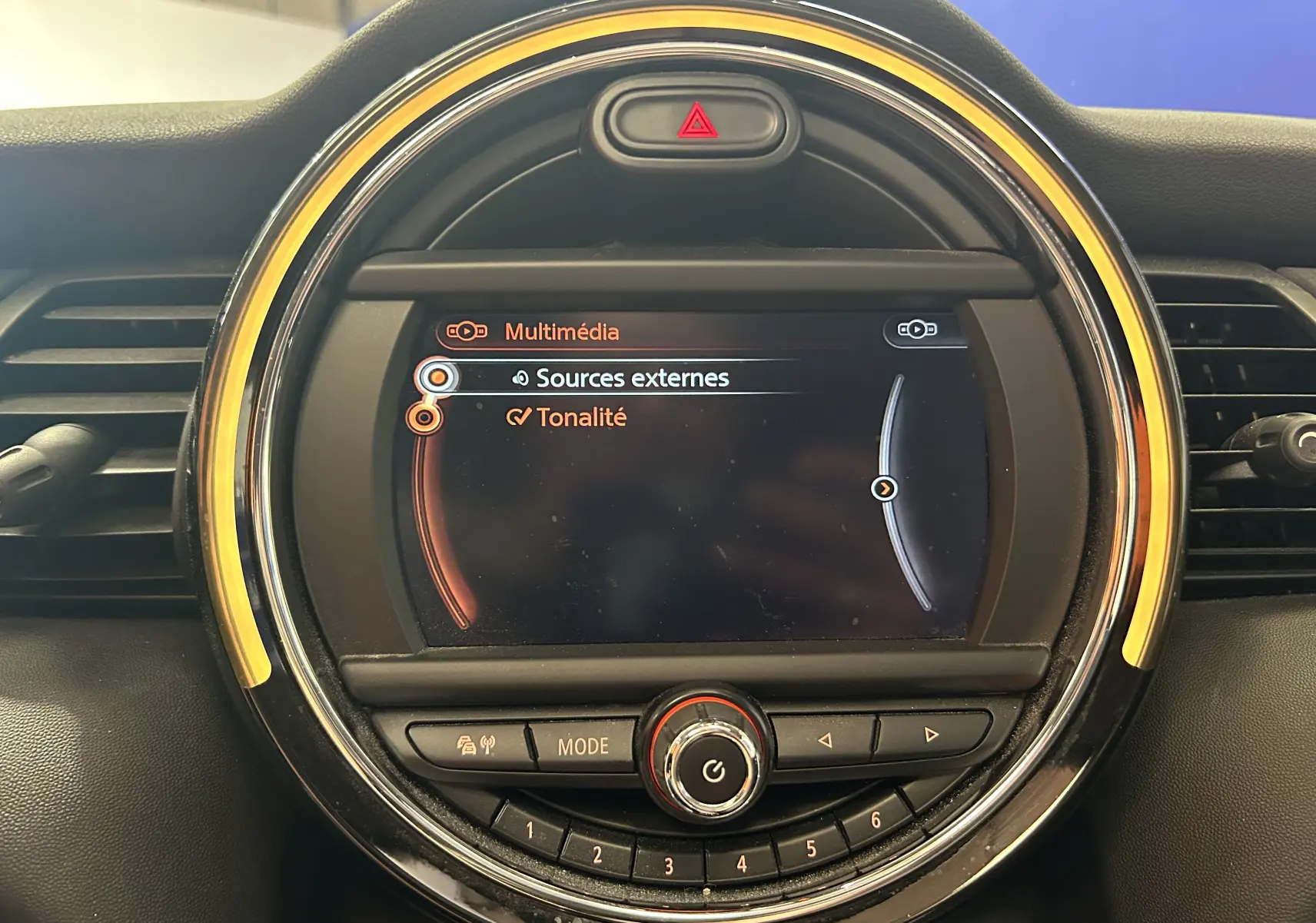 Gros plan sur l'écran multimédia rond du tableau de bord de la MINI 5P Cooper D 2015 avec éclairage orange et commandes intégrées.